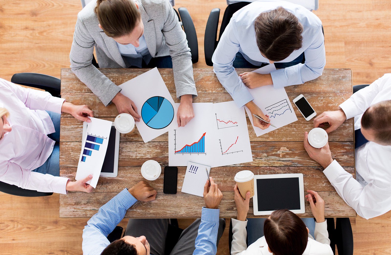 business, people, statistics and team work concept - close up of creative team with charts and gadgets meeting and drinking coffee in office