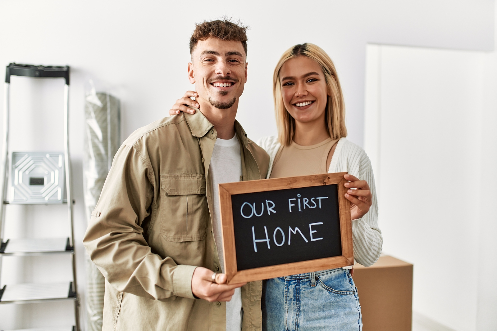 Young caucasian couple smiling happy holding blackboard with our first home message at new house
