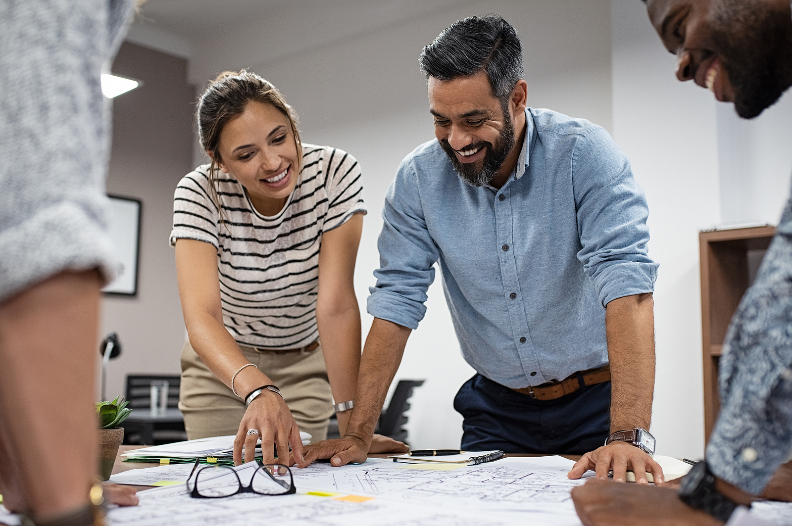 Team of multiethnic architects working on construction plans in meeting room. Engineers discussing on project in office. Mature businessman and woman standing around table working on blueprint.