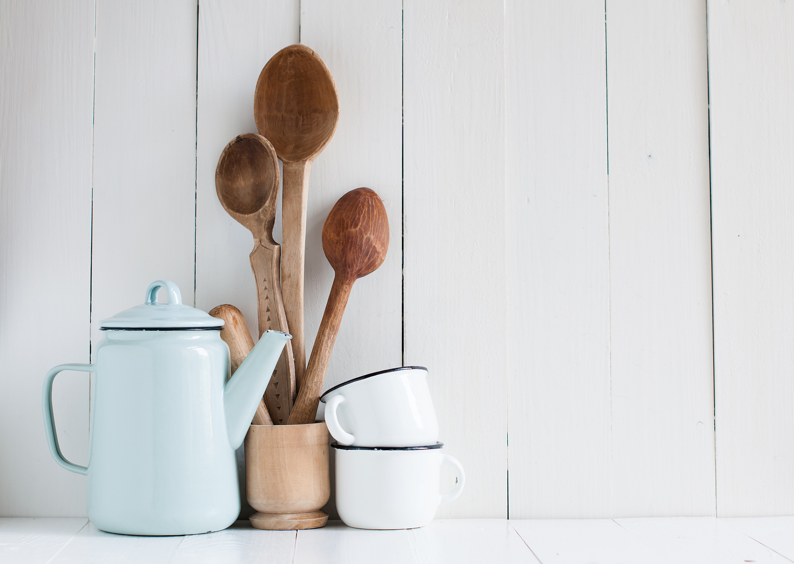 Home kitchen still life: Vintage coffee pot enamel mugs and antique rustic wooden spoons on a barn wall background soft pastel colors.